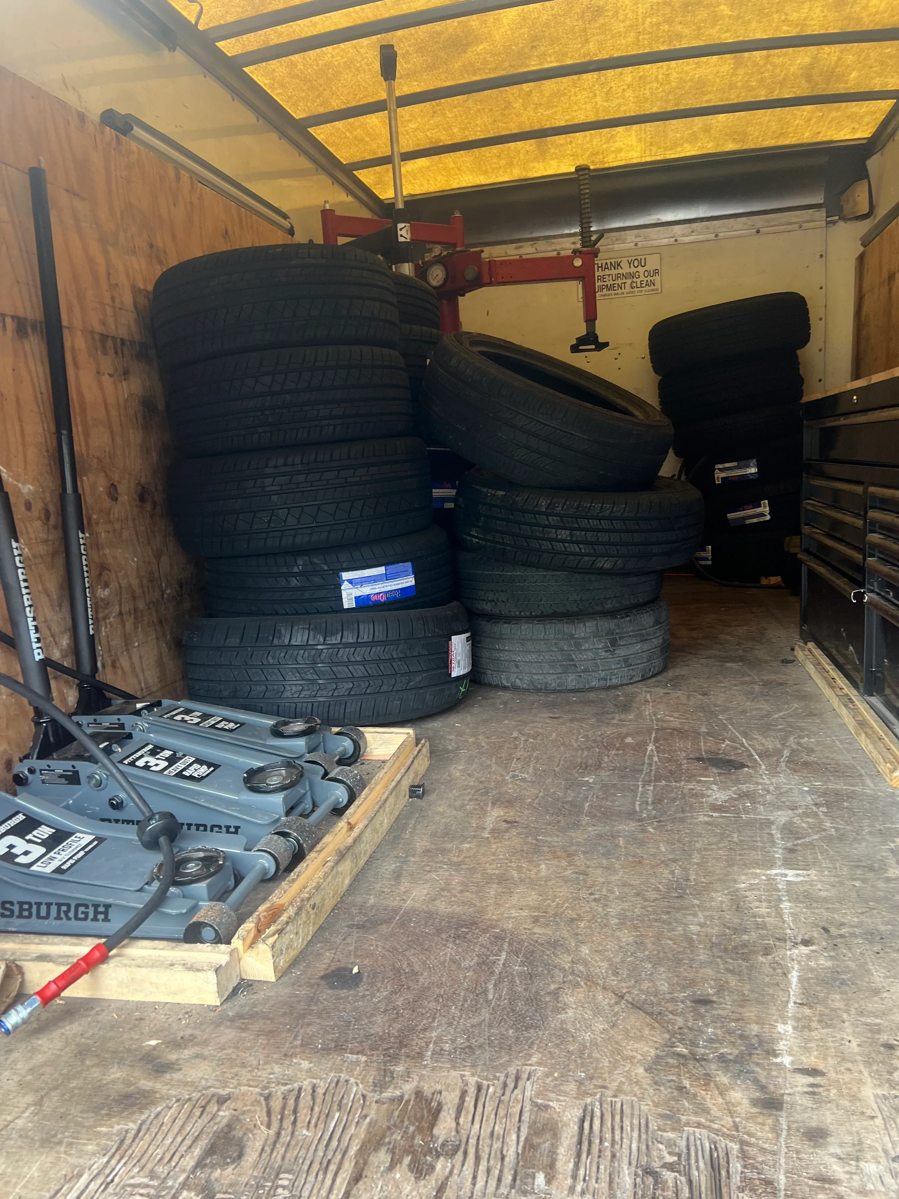 Inside the Nashville Flat Tire Service mobile service truck, fully loaded with stacked replacement tires, multiple Pittsburgh hydraulic floor jacks, and a tool chest used for fleet and on-site dispatch.