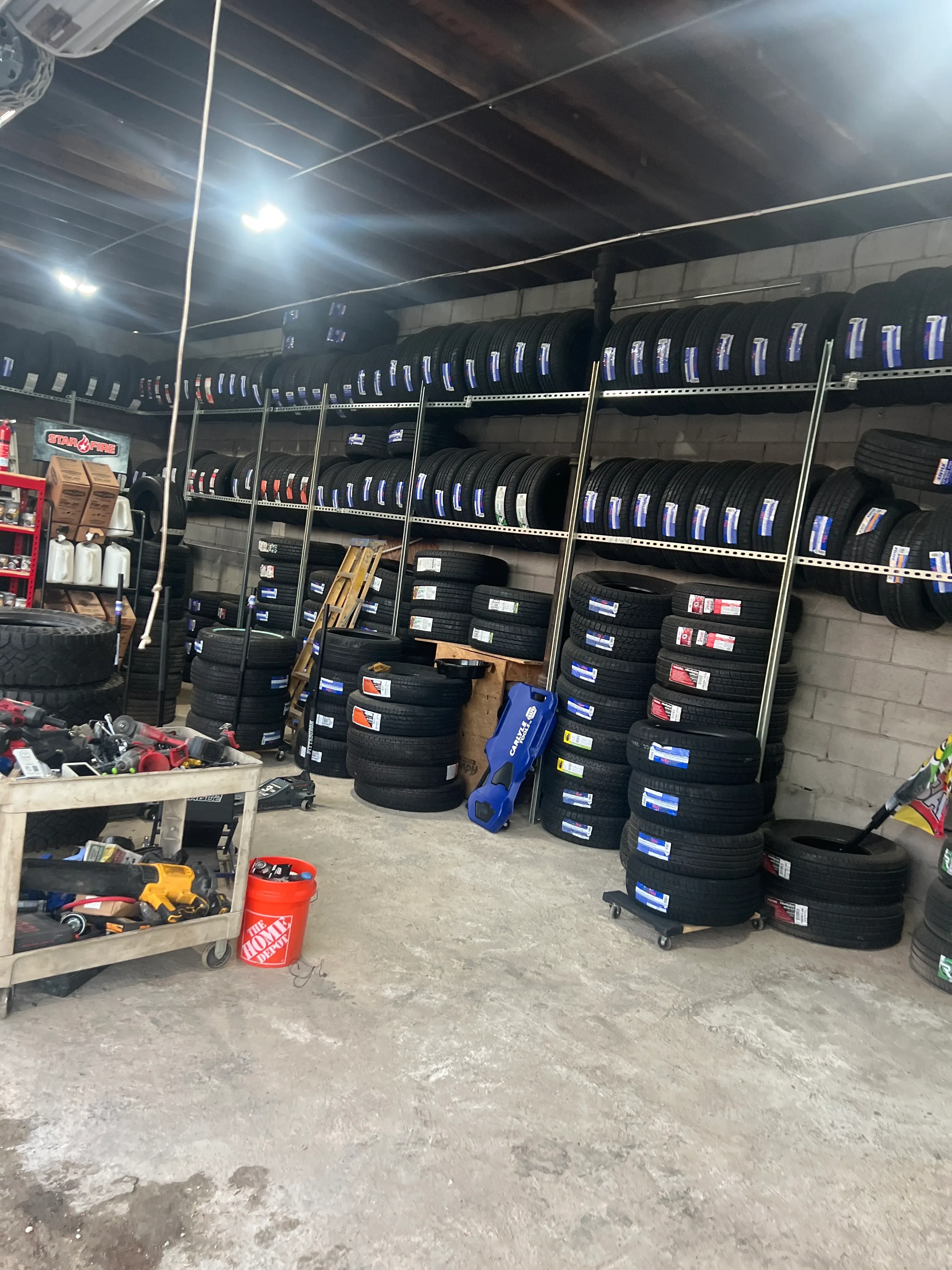Inside the Nashville Flat Tire Service shop, lined with shelves of new passenger and light-truck tires, hydraulic floor jacks, a service cart, and roadside response equipment.