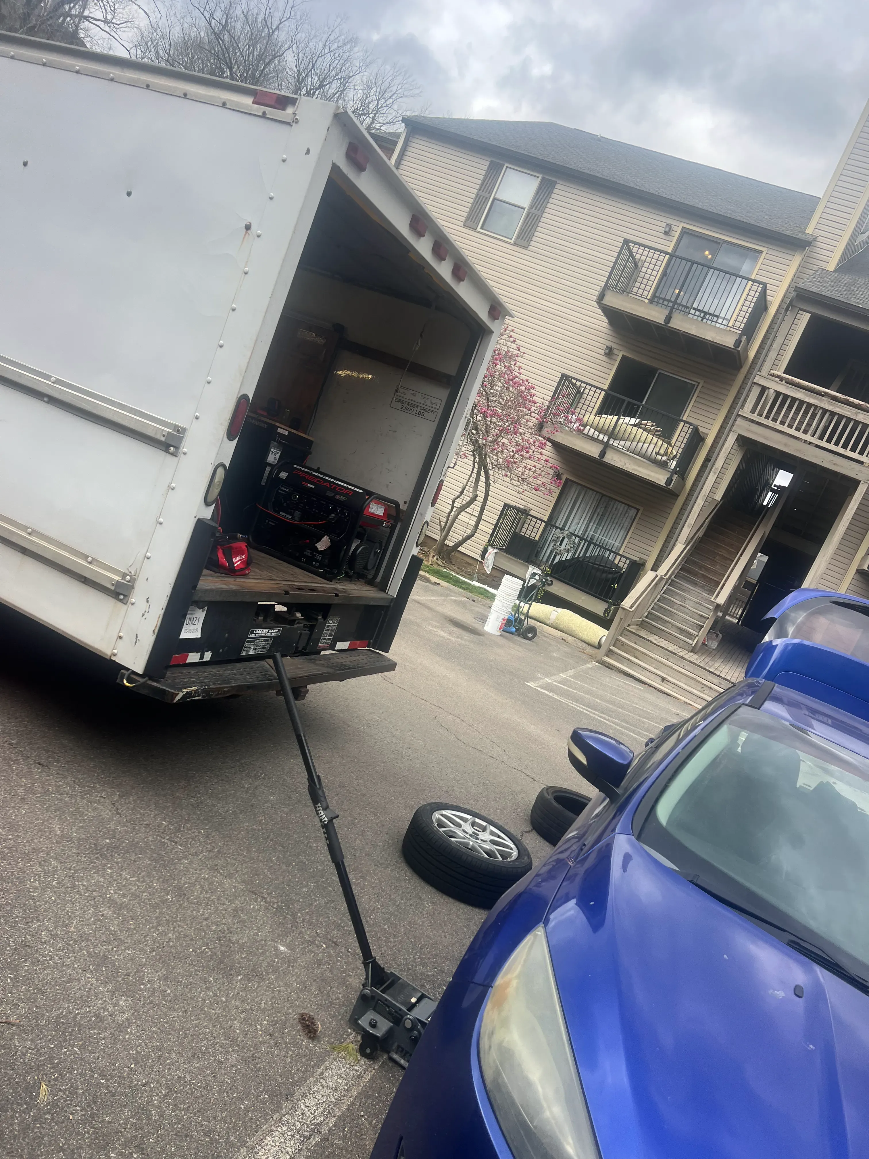 Nashville Flat Tire Service mobile box truck dispatched to a Greater Nashville apartment complex with the rear doors open showing replacement tires, a hydraulic jack, generator, and roadside service equipment ready for a 24/7 call.